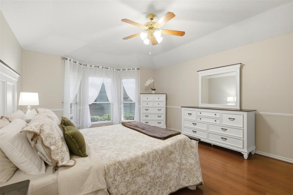 4218 Glistening Spring Rowlett, TX 75088 - Photo 19 of 39 Hardwood-style flooring in a light-filled bedroom featuring a bay window, ceiling fan with integrated lighting, and neutral wall tones with decorative molding