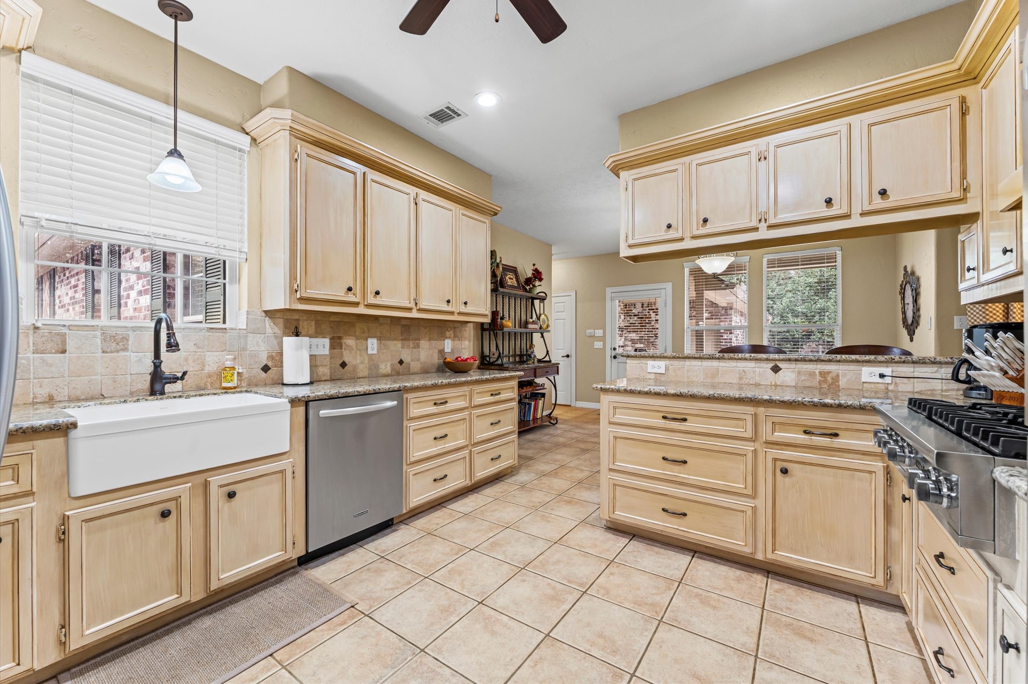 22625 Tomball Cemetery Road Tomball, TX 77377 - Photo 11 of 32 This kitchen features a rustic design with light wood cabinetry, granite countertops, and a farmhouse sink. It includes modern stainless steel appliances, a gas stove, and ample storage space. The room is bright with natural light from large windows and has a cozy, inviting atmosphere.