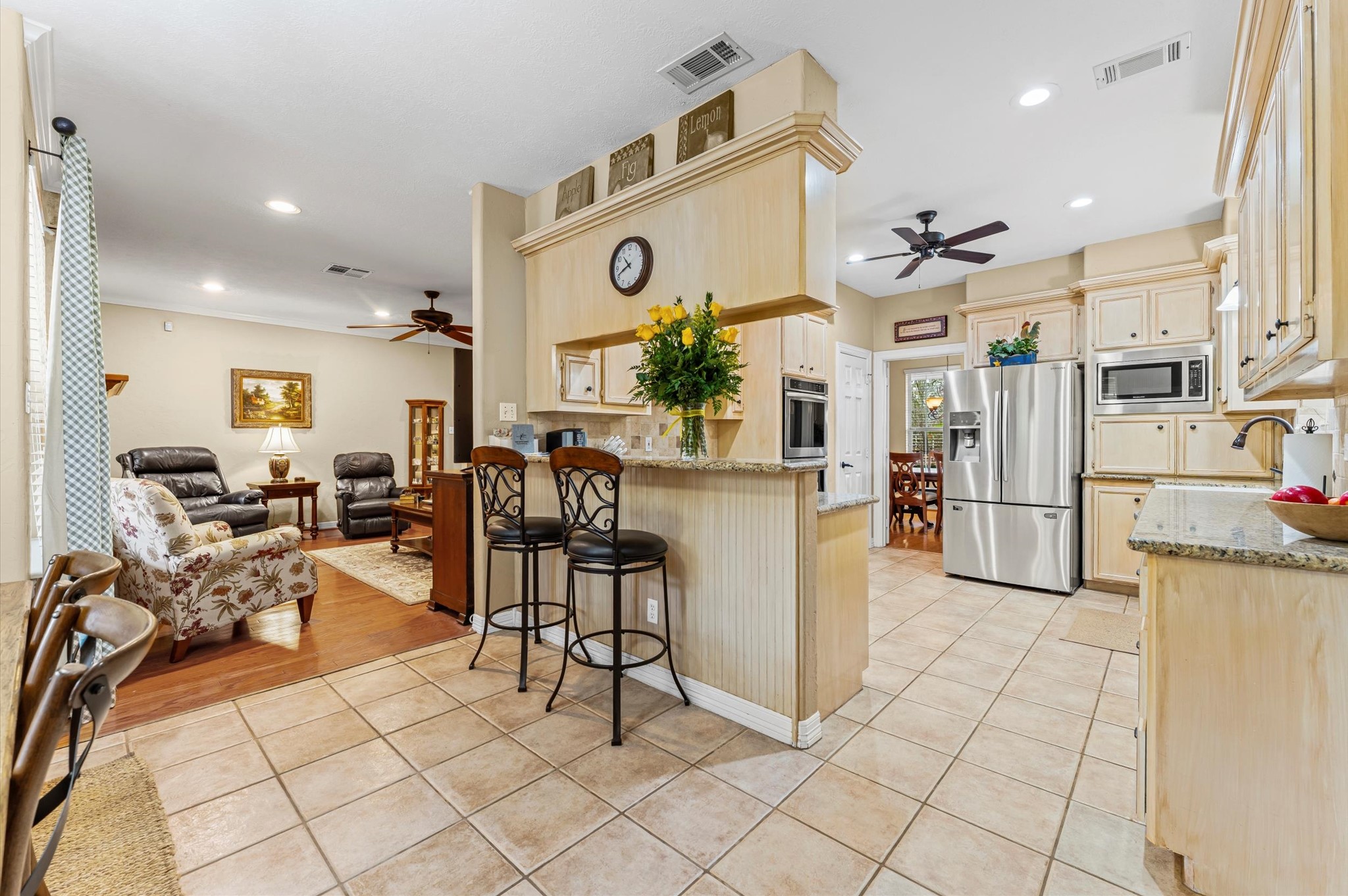 22625 Tomball Cemetery Road Tomball, TX 77377 - Photo 14 of 32 The kitchen features light wood cabinetry, granite countertops, and stainless steel appliances. Adjacent is a cozy living space with wood flooring and comfortable seating. The area is well-lit, combining tiled and hardwood floors for a warm, inviting atmosphere.