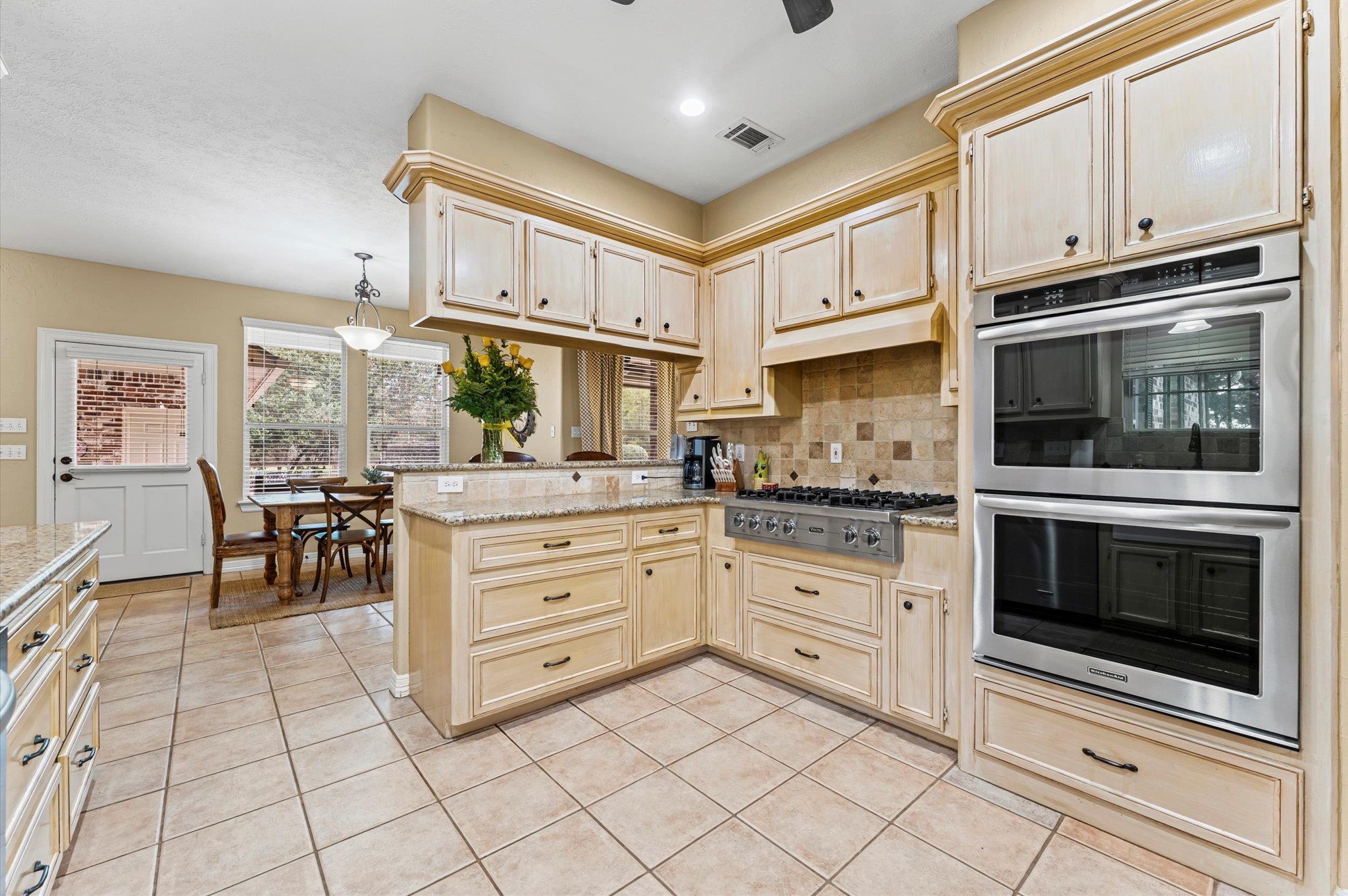 22625 Tomball Cemetery Road Tomball, TX 77377 - Photo 15 of 32 This kitchen features elegant cabinetry, a spacious layout, and stainless steel appliances, including double ovens and a gas cooktop. The dining area offers natural light with large windows, creating a warm and inviting space.
