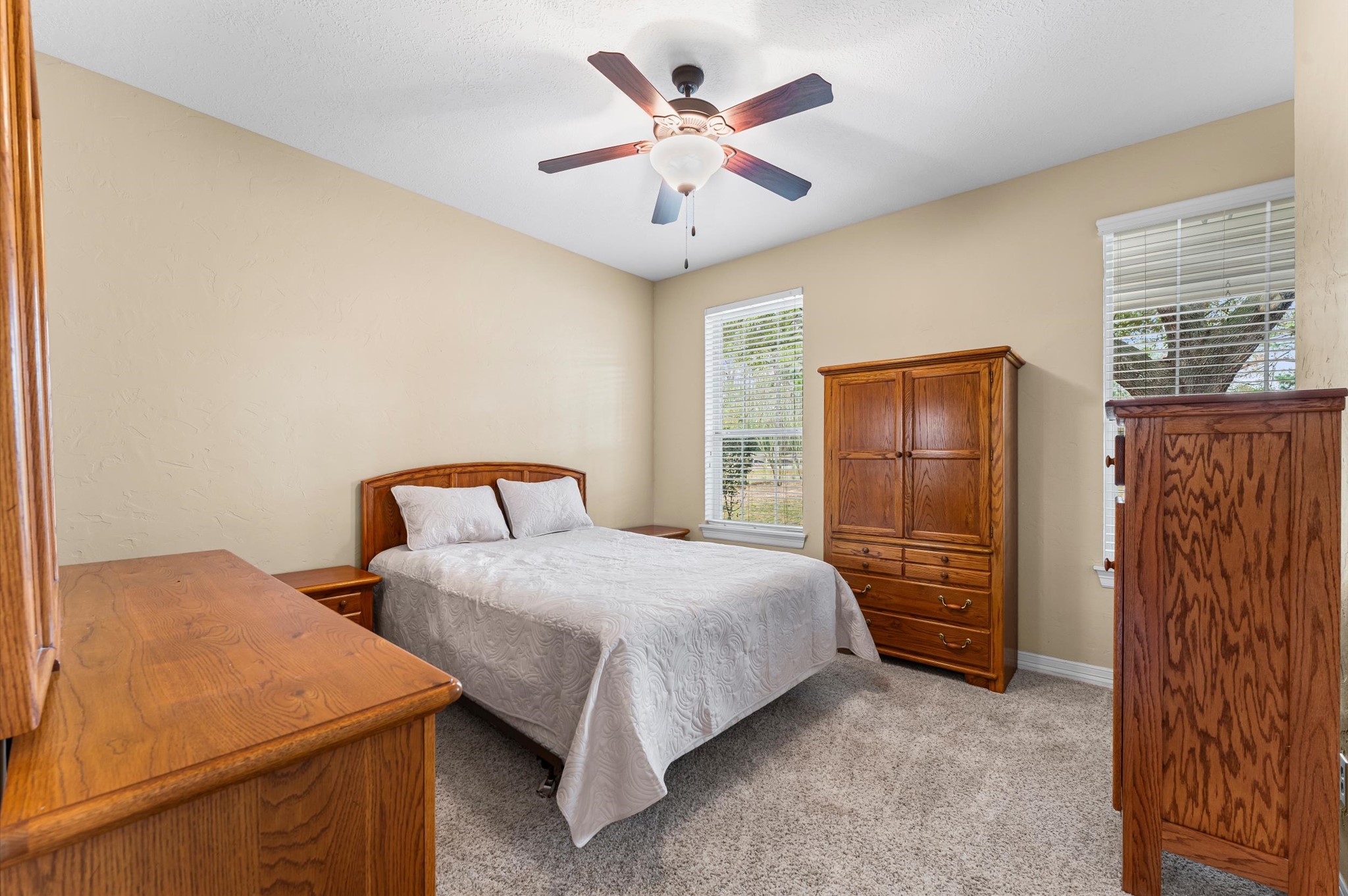 22625 Tomball Cemetery Road Tomball, TX 77377 - Photo 17 of 32 Cozy bedroom with neutral walls and carpeted flooring, featuring a ceiling fan and ample natural light from two windows.