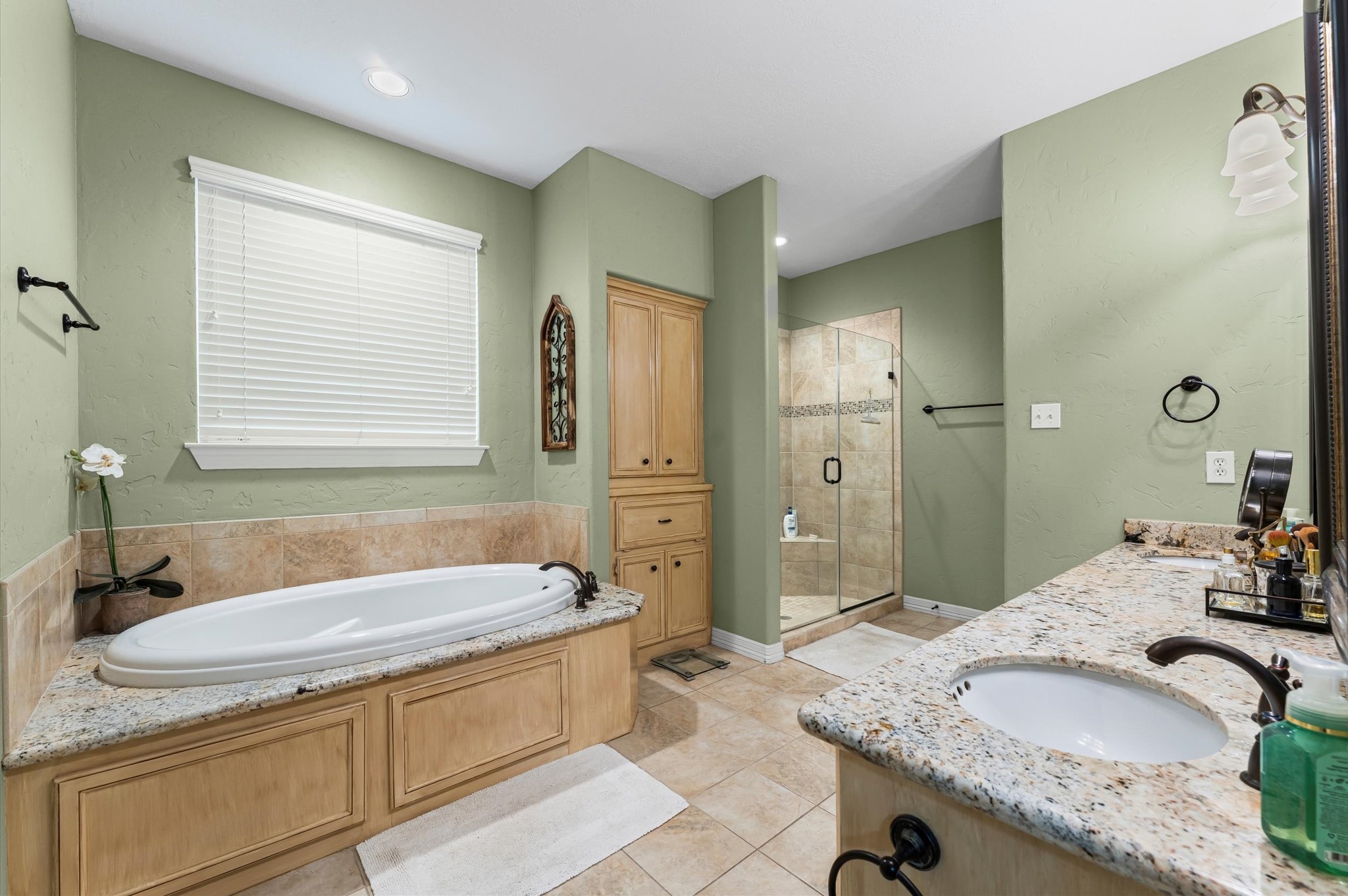 22625 Tomball Cemetery Road Tomball, TX 77377 - Photo 22 of 32 This bathroom features a relaxing spa tub, a modern glass-enclosed shower, and a dual-sink vanity with granite countertops. The soft green walls and natural wood accents create a tranquil atmosphere, perfect for unwinding.