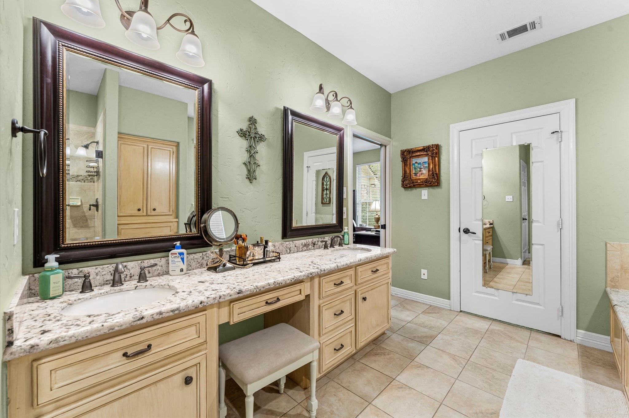22625 Tomball Cemetery Road Tomball, TX 77377 - Photo 24 of 32 This bathroom features a spacious double vanity with granite countertops, large mirrors, elegant light fixtures, and ample storage. The light green walls create a calming atmosphere, complemented by tiled floors and a door with a full-length mirror.