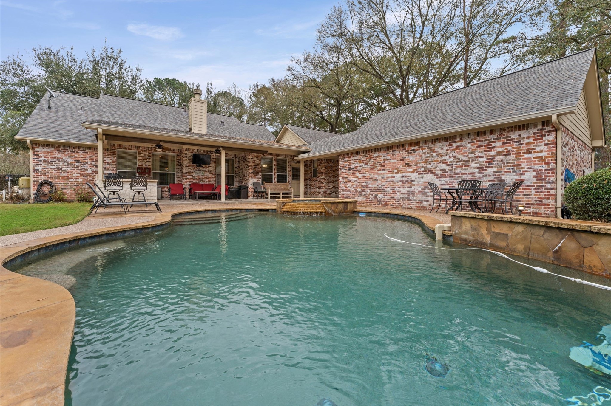 22625 Tomball Cemetery Road Tomball, TX 77377 - Photo 28 of 32 Charming brick home with a spacious backyard featuring a large PebbleTech Pool and patio area. Ideal for outdoor entertaining, with plenty of space for seating and dining areas under a covered section. Surrounded by mature trees for added privacy and tranquility.