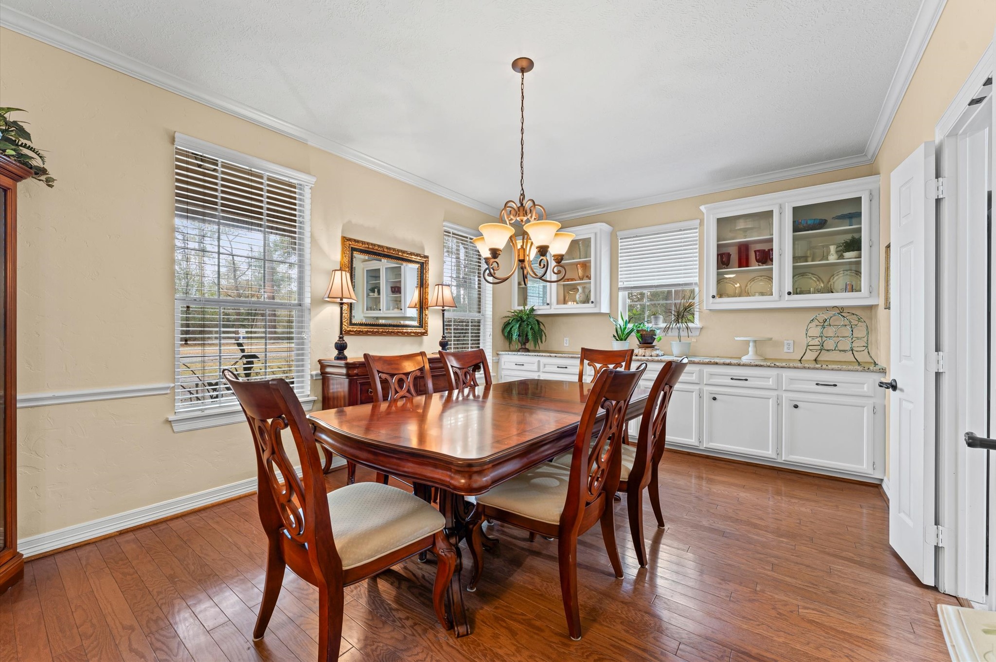22625 Tomball Cemetery Road Tomball, TX 77377 - Photo 7 of 32 This dining room features a warm and inviting atmosphere with hardwood floors. It includes a chandelier, and ample natural light from multiple windows. The white cabinetry offers additional storage and a beautiful display space.