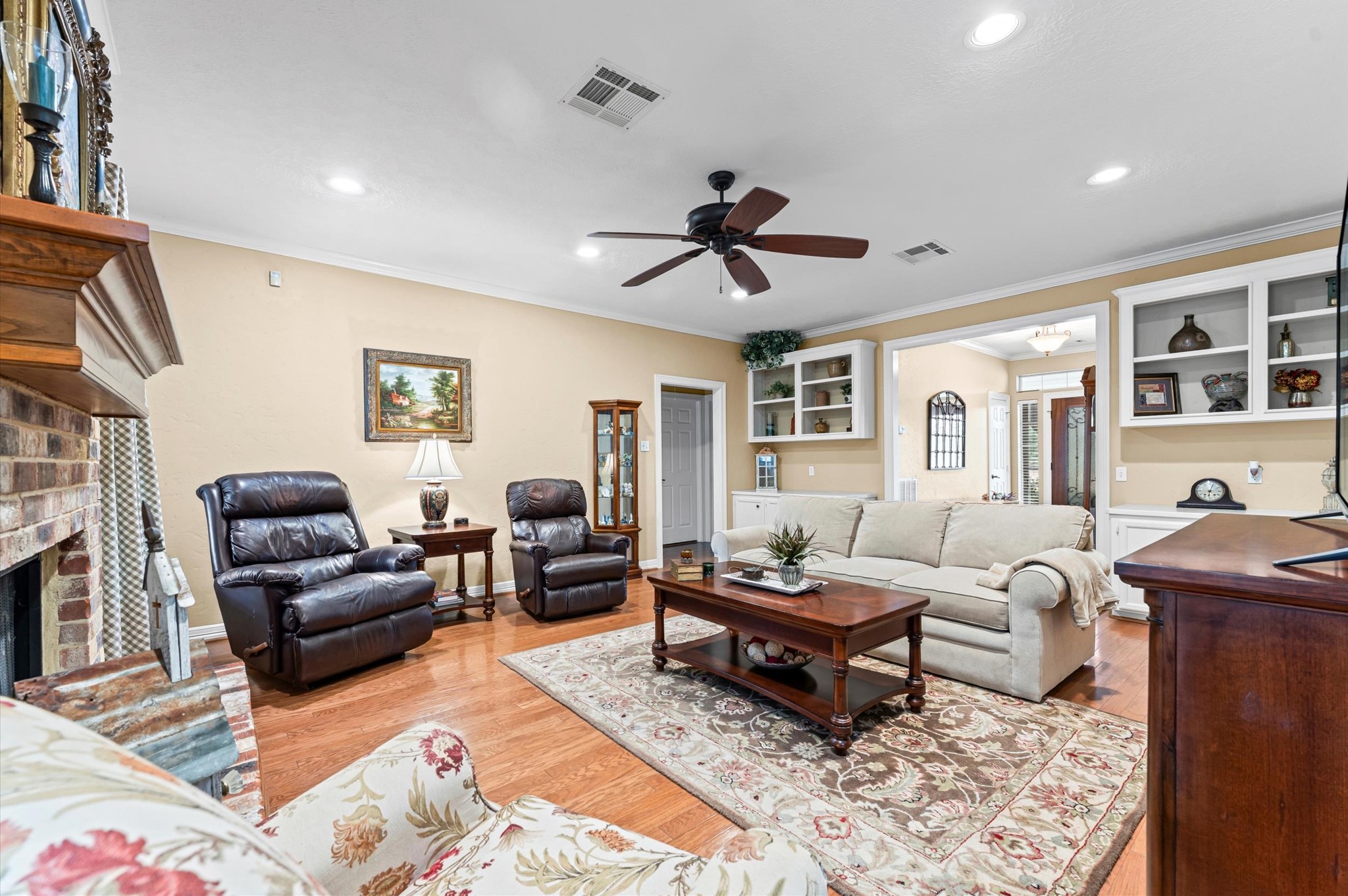 22625 Tomball Cemetery Road Tomball, TX 77377 - Photo 8 of 32 This cozy living room features warm wood flooring, a brick fireplace, and a ceiling fan. It includes plenty of space for comfortable seating and built-in shelving and cabinetry. The space is well-lit and inviting, perfect for relaxation and gatherings.