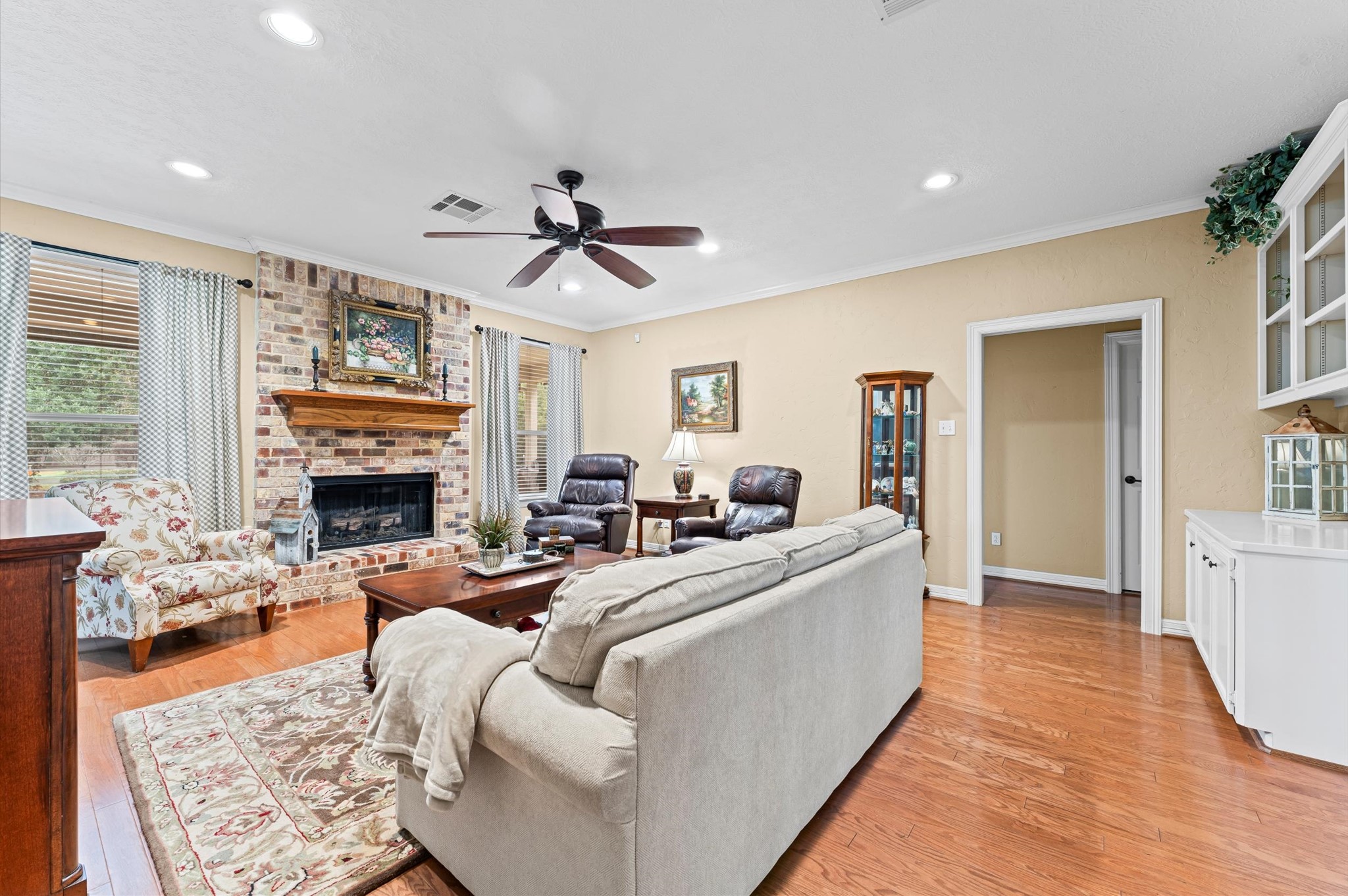 22625 Tomball Cemetery Road Tomball, TX 77377 - Photo 9 of 32 A cozy living room featuring a brick fireplace, hardwood floors, and a ceiling fan with ample natural light from large windows.