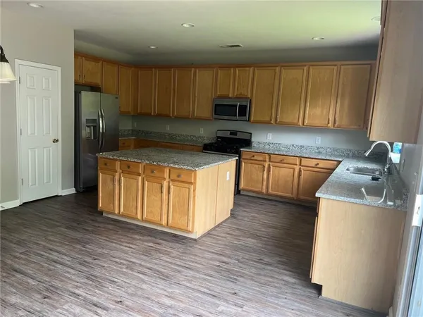 a kitchen with stainless steel appliances granite countertop a stove top oven a refrigerator a sink and dishwasher with wooden floor