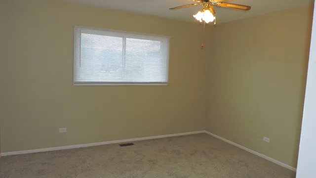 an empty room with a chandelier fan and windows