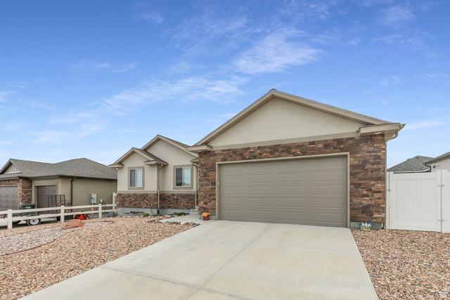 1228 North Providence Way Tooele, UT 84074 - Photo 3 of 28 Front exterior featuring a two-car garage, concrete driveway, stone veneer accents, stucco siding, and a low-maintenance gravel yard