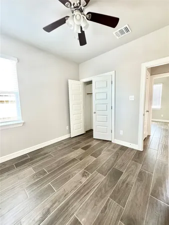 an empty room with wooden floor chandelier fan and windows