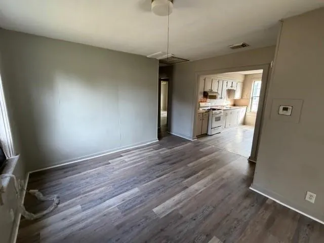 a room with wooden floor and a view of kitchen
