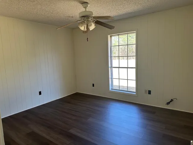 an empty room with wooden floor fan and windows