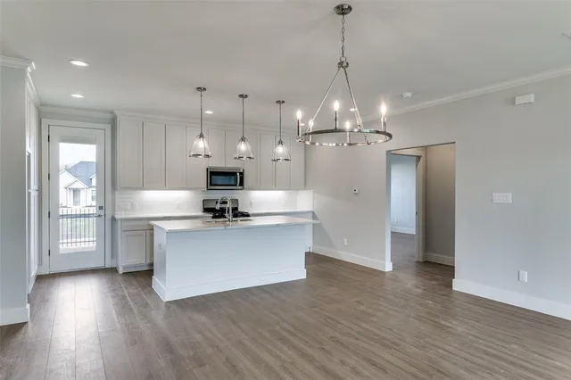 a view of a kitchen with granite countertop wooden floor stainless steel appliances and a chandelier