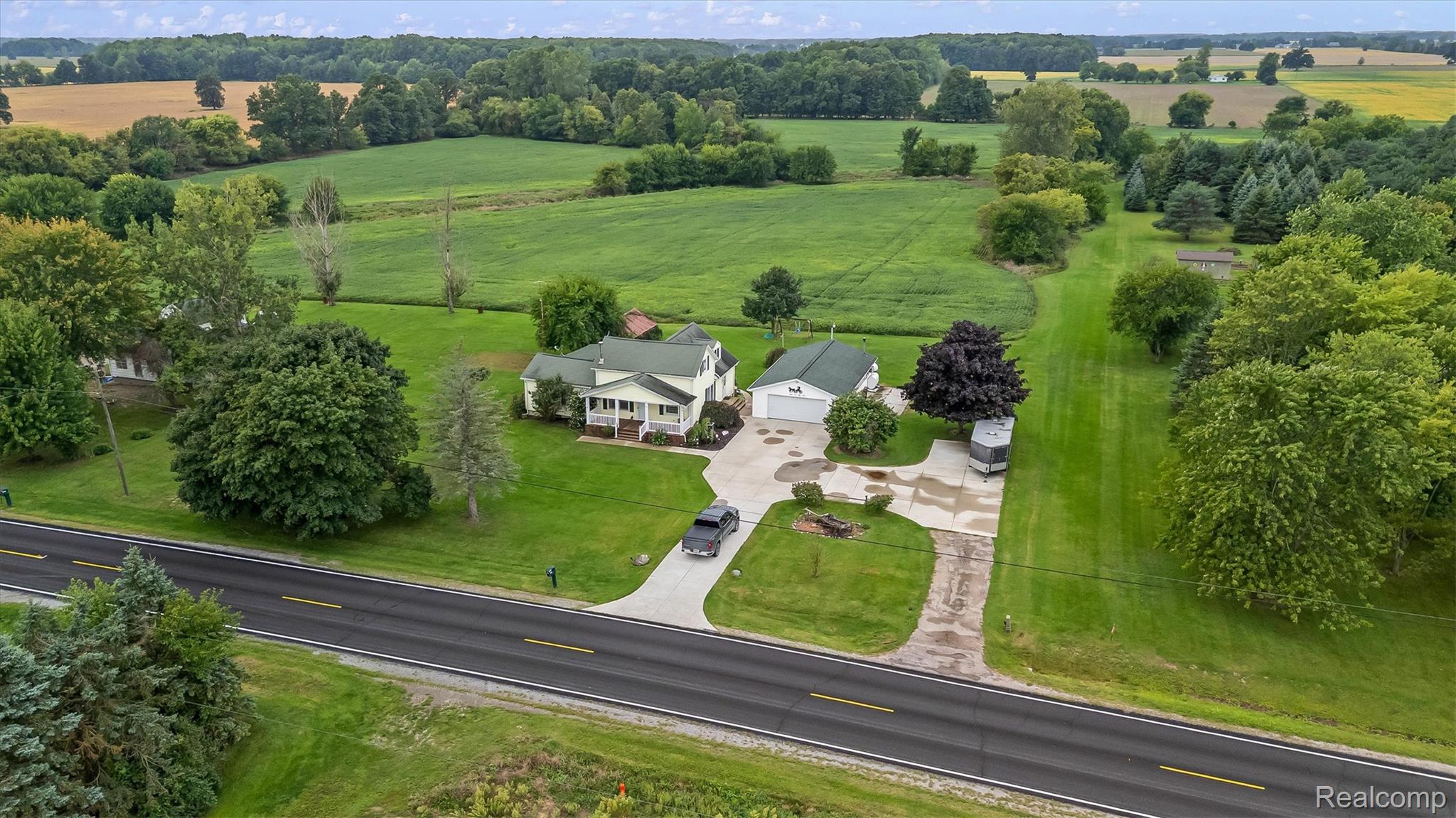 3553 North State Road Owosso, MI 48867 - Photo 42 of 45 Expansive rural property featuring a primary residence with a covered porch, a separate garage structure, a dedicated paved driveway, and established trees set against a backdrop of open fields