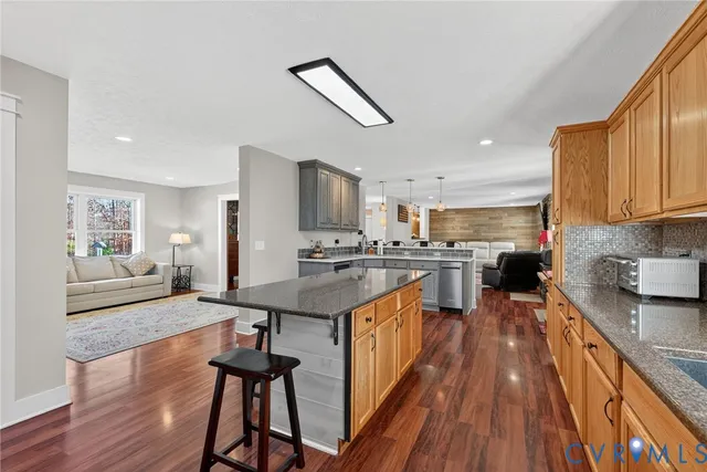 a open kitchen with stainless steel appliances granite countertop a stove top oven a refrigerator a sink dishwasher and a dining table with wooden floor