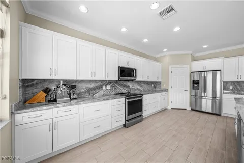 a large white kitchen with stainless steel appliances granite countertop a stove a sink a refrigerator and white cabinets with wooden floor