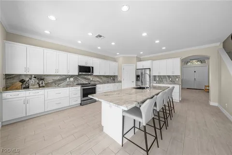 a kitchen with stainless steel appliances kitchen island granite countertop a stove a sink a refrigerator and white cabinets with wooden floor