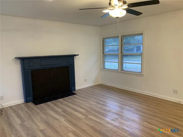 a view of an empty room with wooden floor fireplace and a window