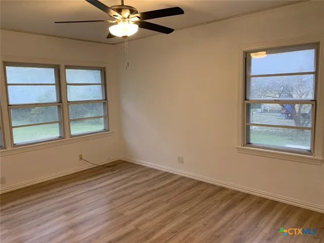an empty room with wooden floor fan and windows