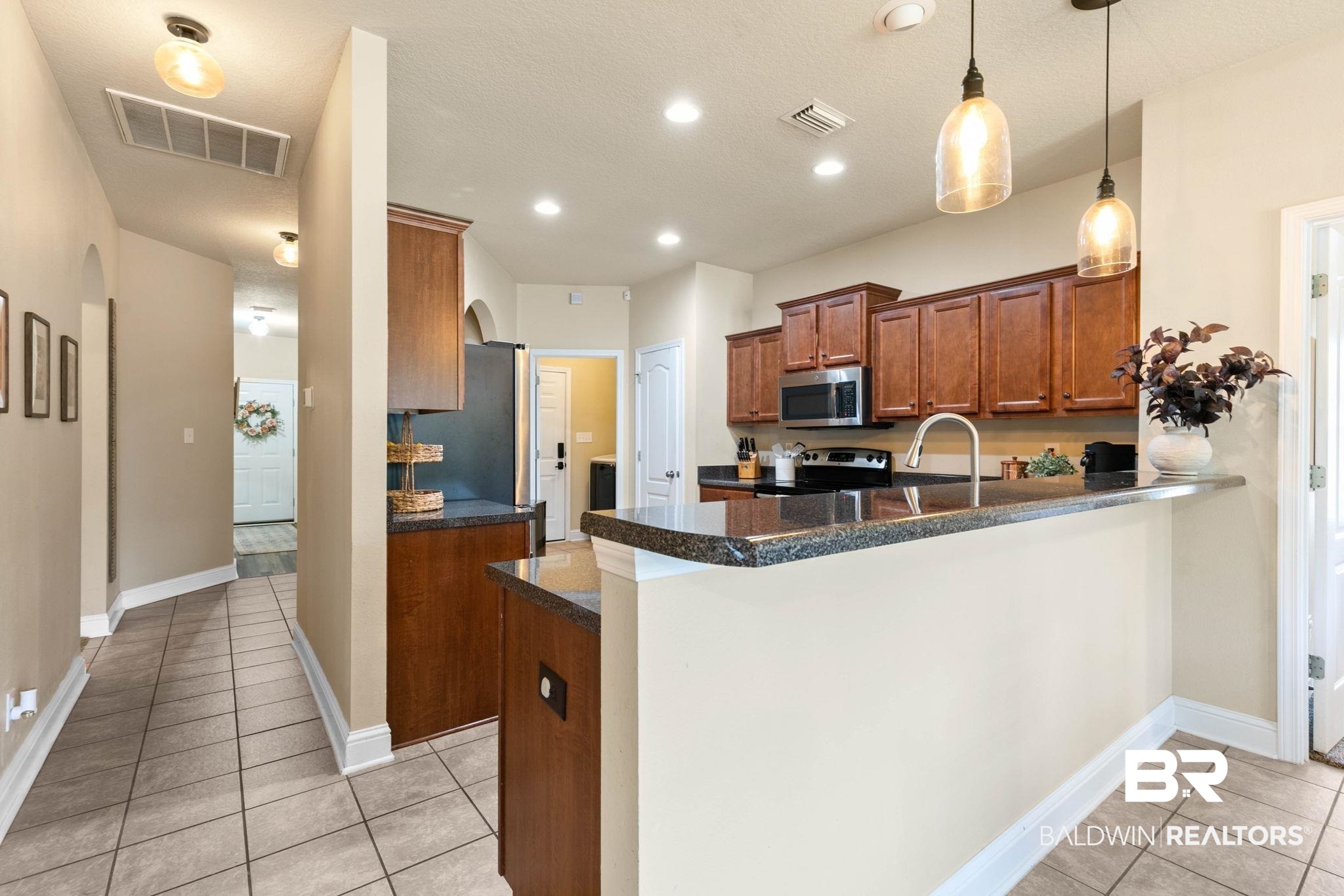 2216 Livingstone Court Mobile, AL 36695 - Photo 11 of 62 Kitchen featuring a raised breakfast bar with stone countertops, dark wood cabinetry, stainless steel appliances, and two pendant light fixtures