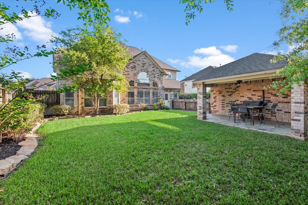 6507 Quiet Pointe Drive Spring, TX 77389 - Photo 28 of 46 Spacious backyard with lush grass, mature trees, and a charming covered patio area perfect for outdoor dining. The brick exterior of the home and privacy fence enhance the inviting atmosphere.