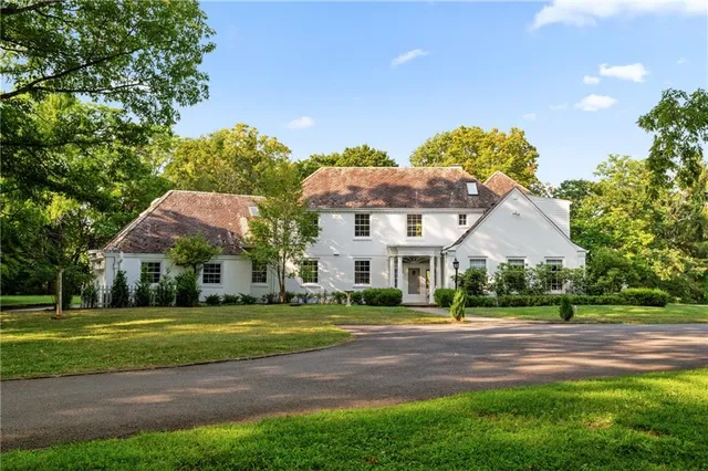 a view of a white house with a big yard and potted plants and large trees