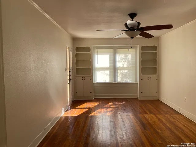 an empty room with wooden floor fan and windows