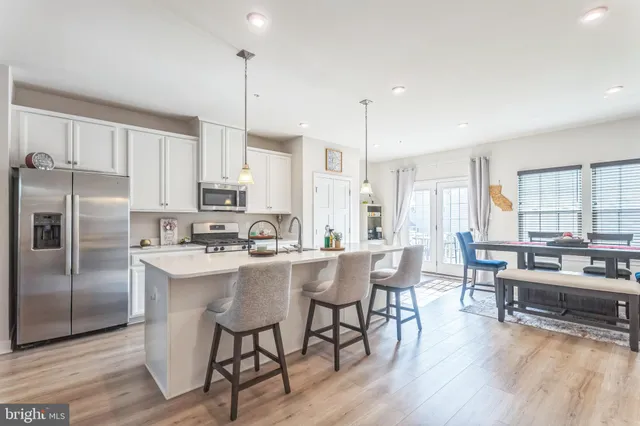 a kitchen with stainless steel appliances granite countertop a stove a refrigerator a kitchen island a dining table and chairs with wooden floor
