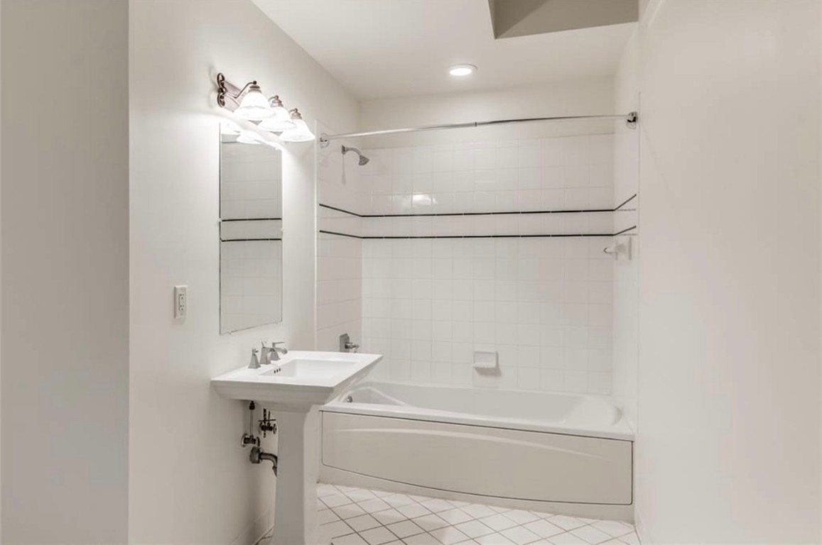 201 Main Street, Unit 6G Houston, TX 77002 - Photo 7 of 14 The primary bathroom offers a deep soaking tub and classic pedestal sink, set against crisp white tile for a clean, timeless look that's ready for your personal touch.