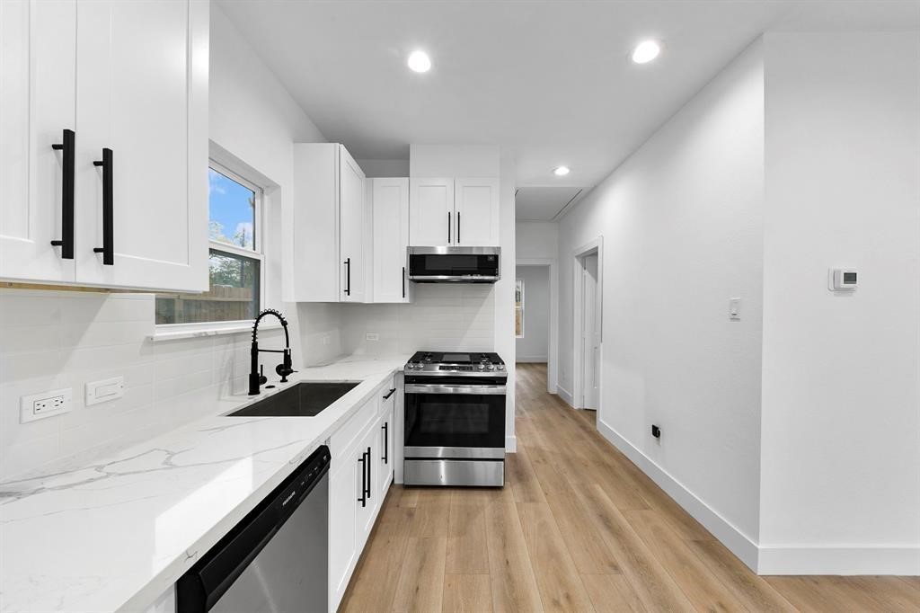 2805 Nettleton Street Houston, TX 77004 - Photo 7 of 9 This photo showcases a modern kitchen featuring sleek white cabinetry, marble countertops, a stainless steel oven, and a dishwasher. The space is well-lit with recessed lighting and has stylish black fixtures, creating a clean and contemporary look.