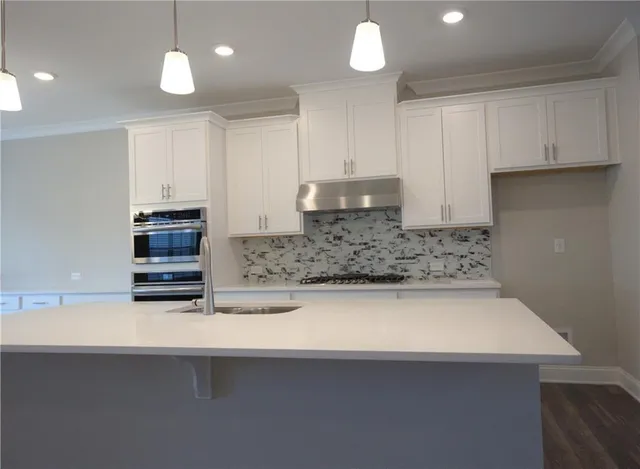 a large kitchen with stainless steel appliances a large island oven a sink dishwasher and a dining table with wooden floor