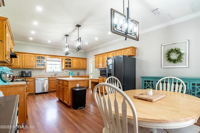 a kitchen with stainless steel appliances kitchen island granite countertop a refrigerator a stove top oven a dining table and chairs with wooden floor