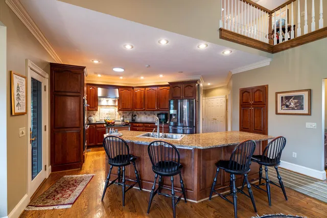 a kitchen with stainless steel appliances granite countertop a refrigerator a sink dishwasher a stove and a dining table with wooden floor