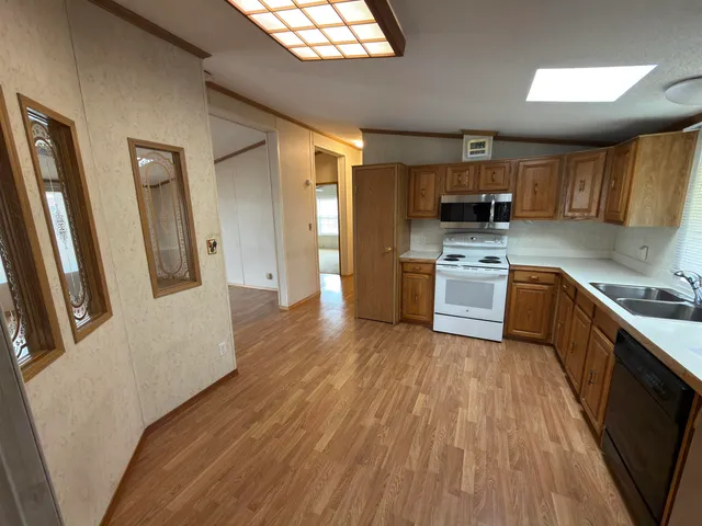 a kitchen with stainless steel appliances granite countertop a refrigerator a sink dishwasher a stove and white countertops with wooden floor