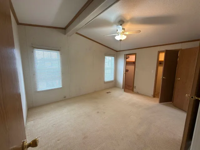 an empty room with chandelier fan and windows