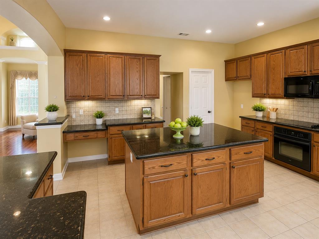 5708 Rickshaw Lane Plano, TX 75094 - Photo 11 of 28 Kitchen featuring a central island with countertop, extensive wood cabinetry, dark countertops, built-in black appliances, and tile flooring