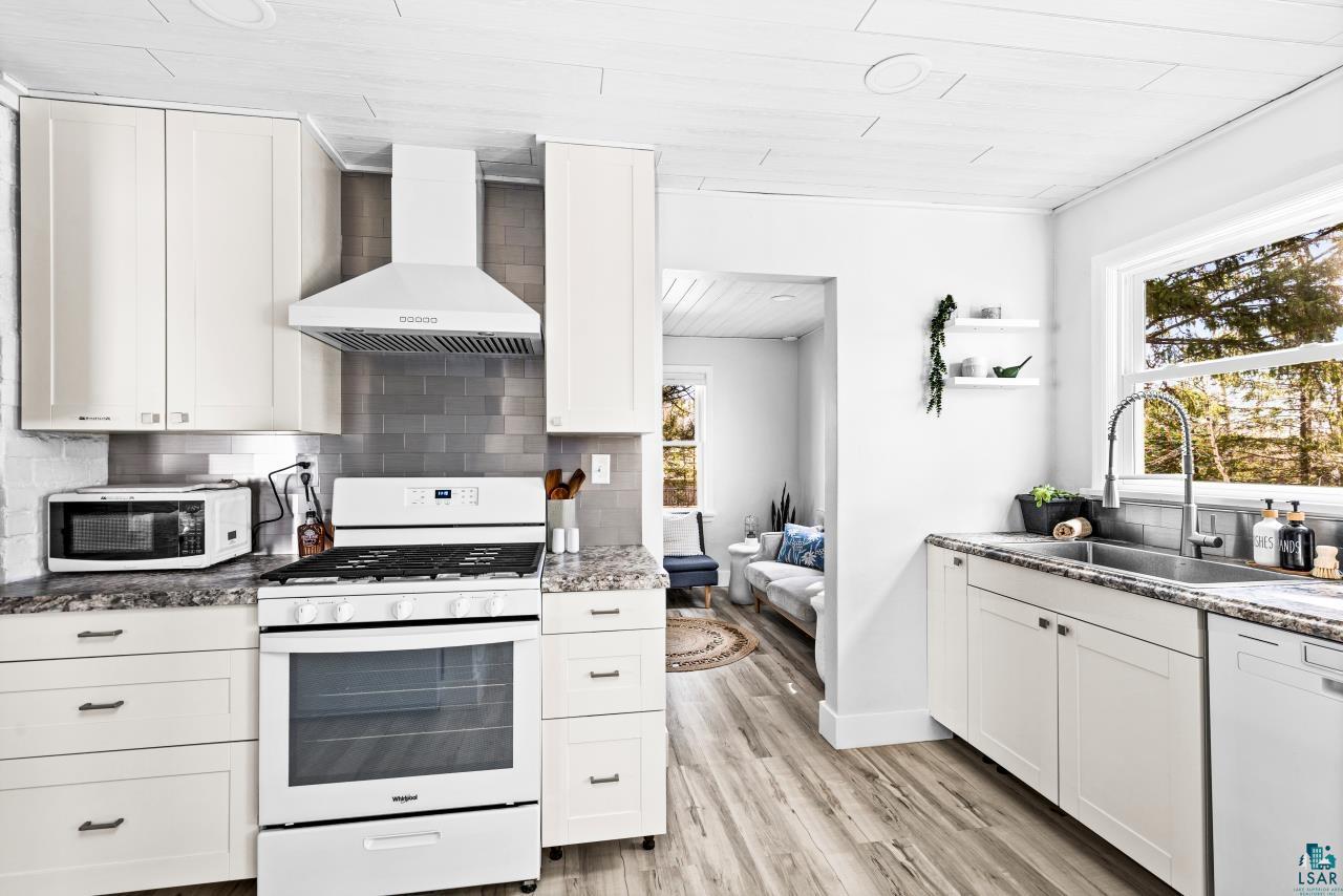 3645 Haines Road Hermantown, MN 55811 - Photo 25 of 35 Kitchen featuring white cabinetry, wood-finish flooring, a stainless steel sink with a gooseneck faucet, a white range with a matching range hood, and a subway tile backsplash