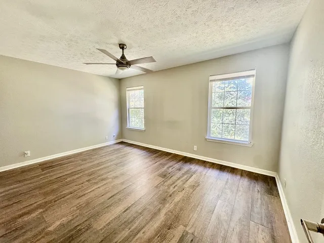 an empty room with wooden floor chandelier fan and windows