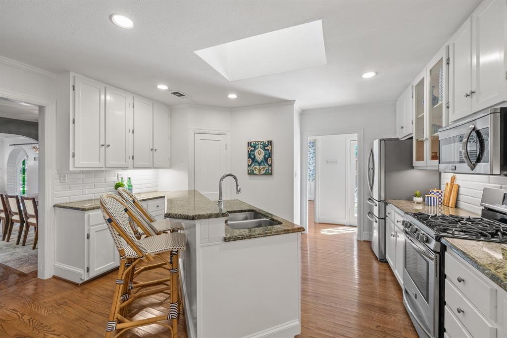 5242 Merrimac Avenue Dallas, TX 75206 - Photo 13 of 25 Kitchen with tasteful backsplash, appliances with stainless steel finishes, white cabinetry, dark stone counters, and dark wood finished floors
