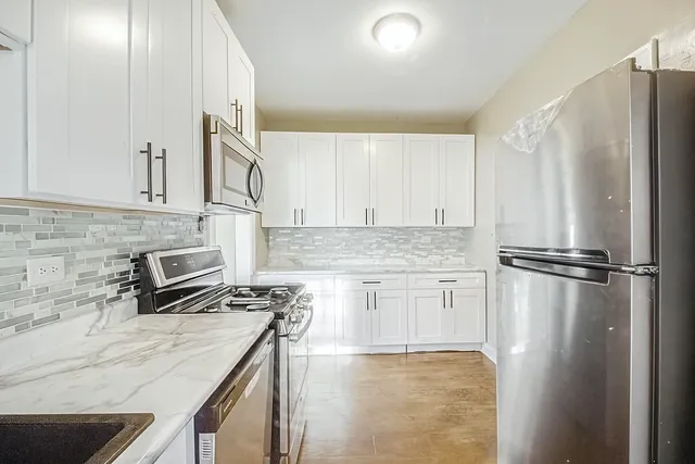 a kitchen with stainless steel appliances granite countertop a refrigerator a stove and white cabinets