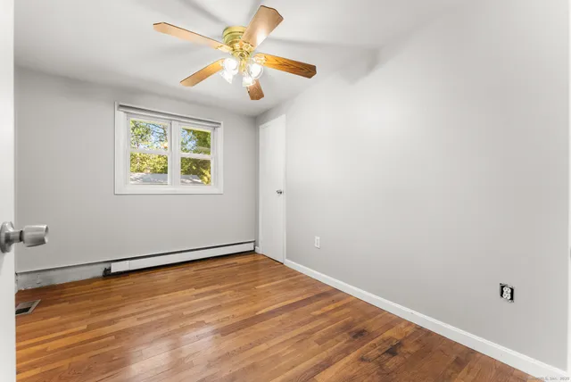 an empty room with wooden floor chandelier fan and windows