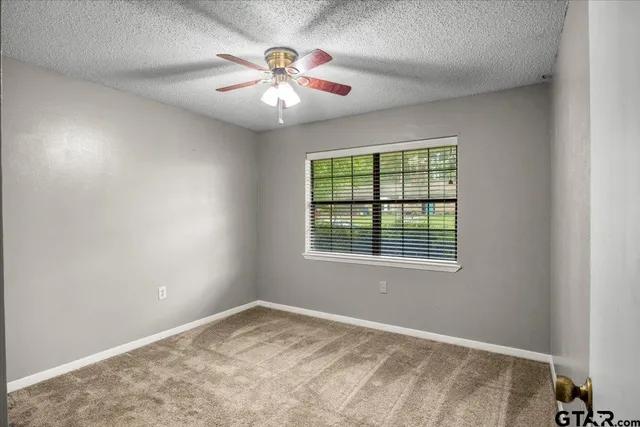 an empty room with chandelier fan and windows