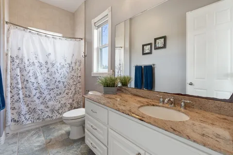 a bathroom with a granite countertop toilet a sink and a mirror