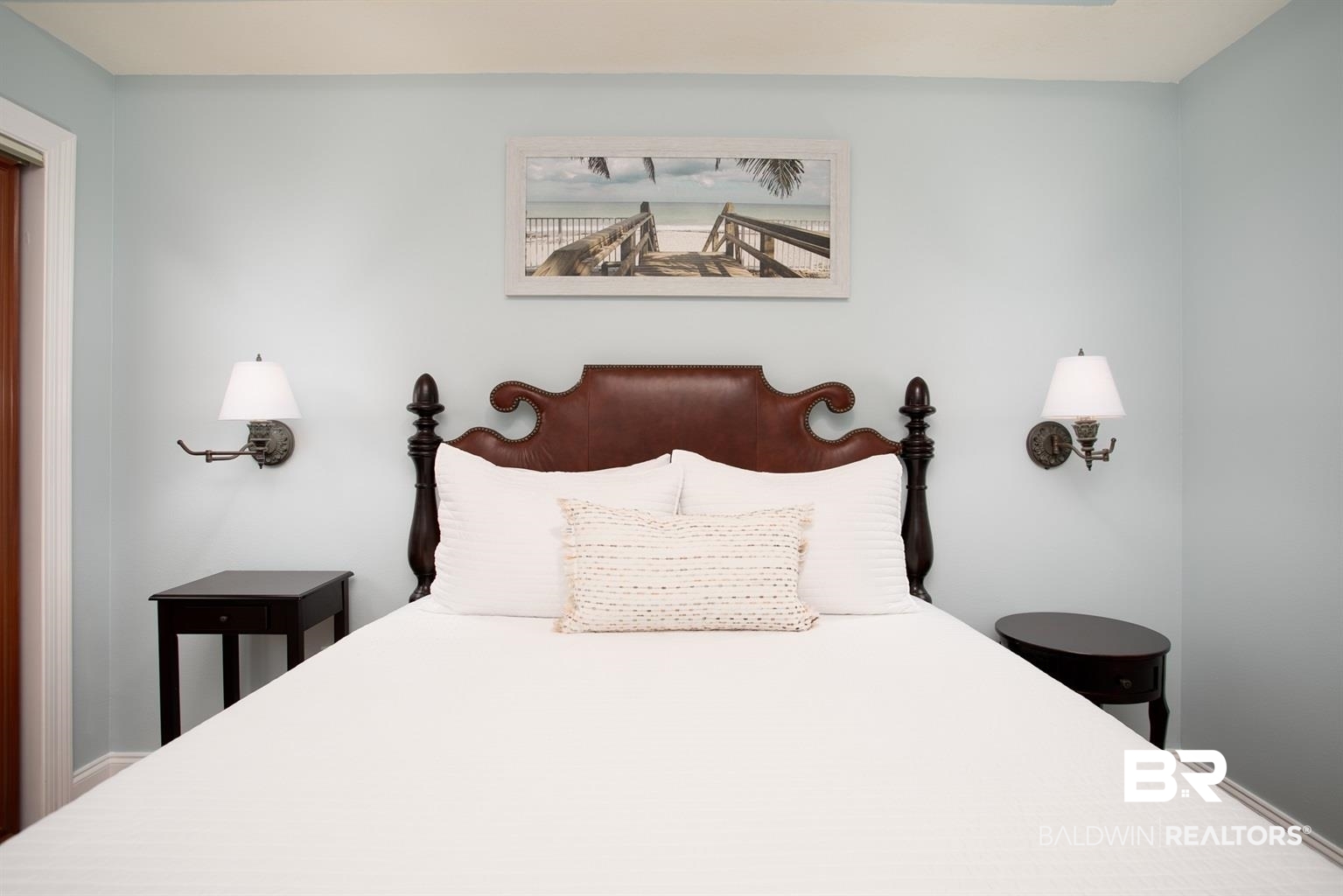27800 Canal Road, Unit 411 Orange Beach, AL 36561 - Photo 17 of 49 Bedroom featuring a dark wood bed frame with a brown upholstered headboard, pale blue walls, and white trim