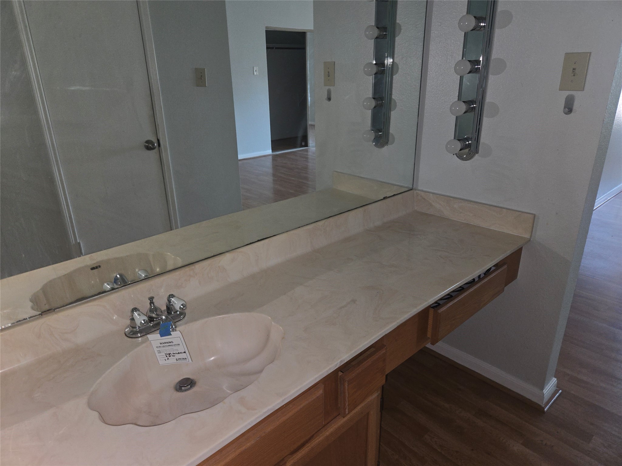 3780 Tanglewilde Street, Unit 501 Houston, TX 77063 - Photo 13 of 26 This photo shows a bathroom vanity with a single sink, a large mirror, lighting fixtures, and a wood-finished countertop. The room has a light color scheme and is adjacent to a space with hardwood flooring.