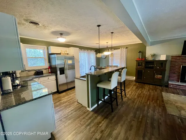 a kitchen with stainless steel appliances kitchen island granite countertop a stove a refrigerator a sink a dining table and chairs with wooden floor