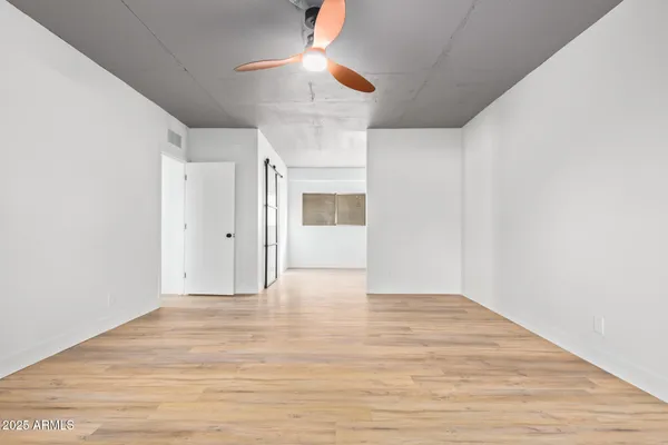 a view of an empty room with wooden floor ceiling fan