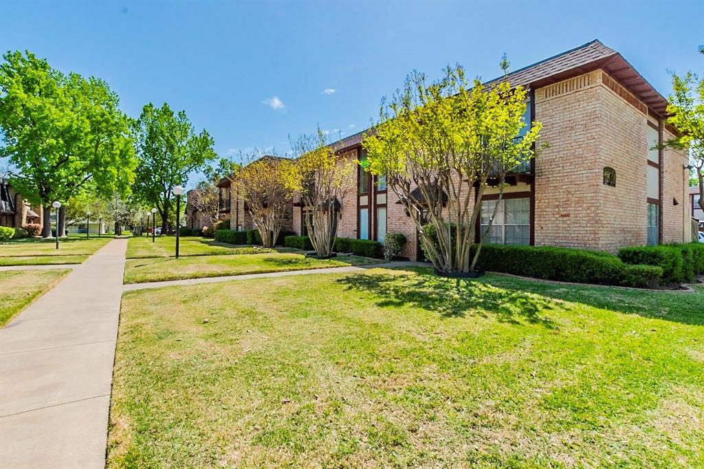 1821 East Grauwyler Road, Unit 188 Irving, TX 75061 - Photo 20 of 20 Brick exterior building with a brown shingle roof, featuring multiple windows and surrounding green landscaping