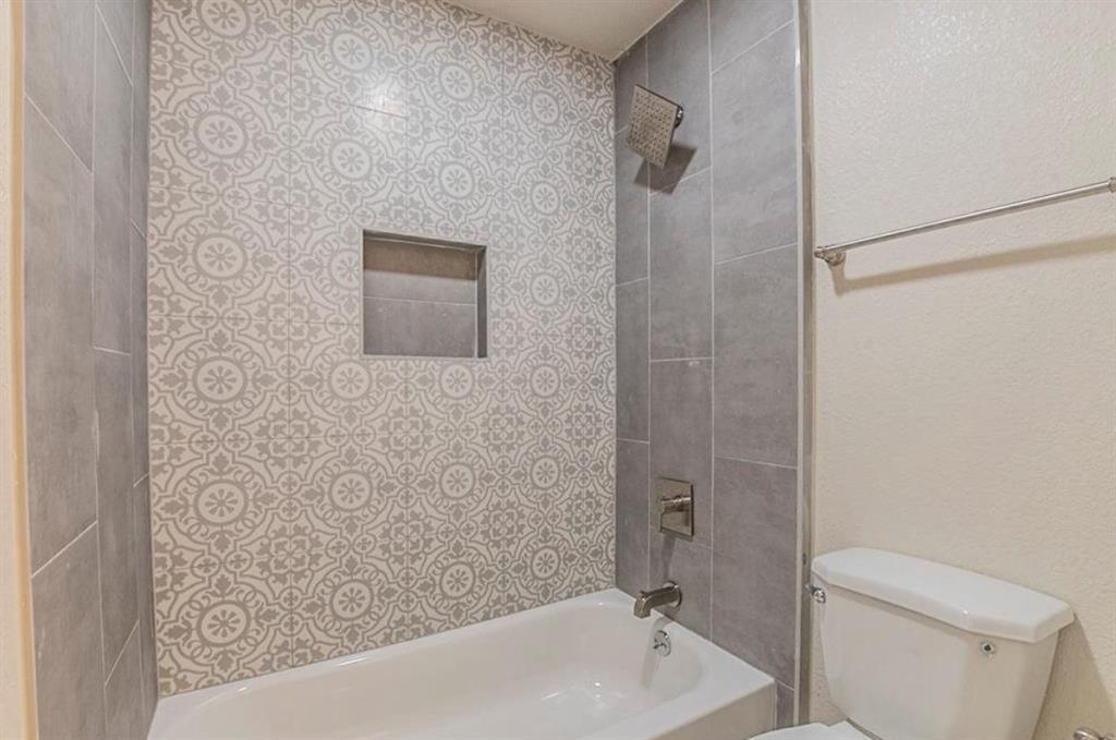 1821 East Grauwyler Road, Unit 188 Irving, TX 75061 - Photo 9 of 20 Tiled shower and tub combination featuring patterned and solid gray wall tiles, a built-in shower niche, and brushed nickel fixtures
